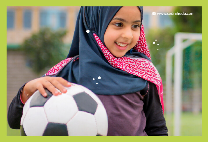 طفلة محجبة ومبتسمة تمسك كرة القدم.